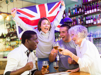 Happy sport fans holding flag of the Great Britain, celebrating victory of national team, drinking alcoholic drinks in beer pub