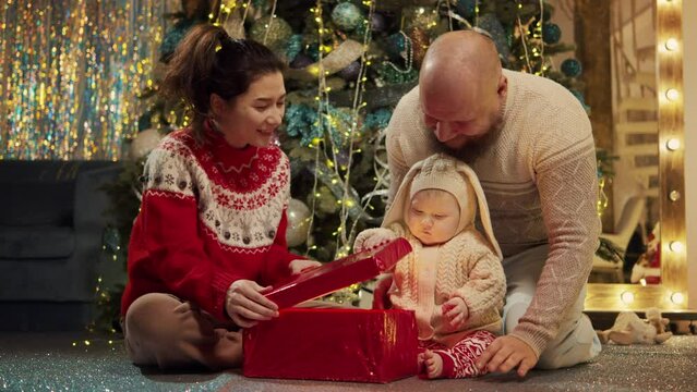 Family and sweet little asian baby boy at background of decorated fir-tree open box with surprise of Christmas. Happy mom dad unpack present or gift. Merry xmas, happy new year loving parents concept