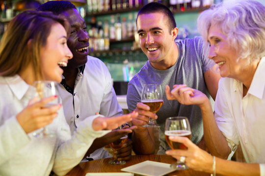 Diverse people talking and laughing drinking beer at a bar table. High quality photo