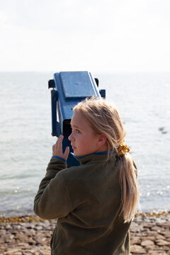 Girl looks whistfully along the shore. She is holding a binocular.