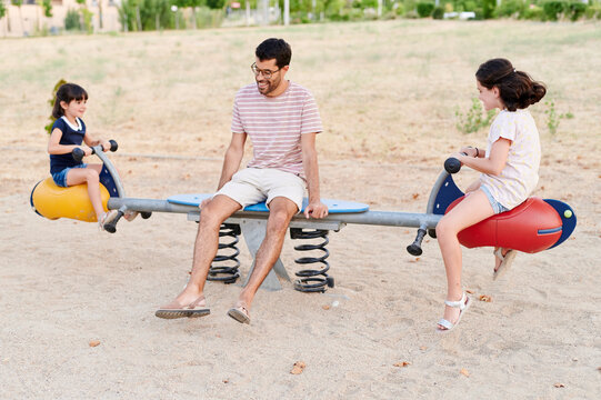 Laughing uncle and nieces playing on a seesaw