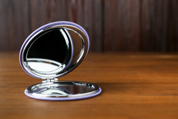 Stylish cosmetic pocket mirror on wooden table. Space for text