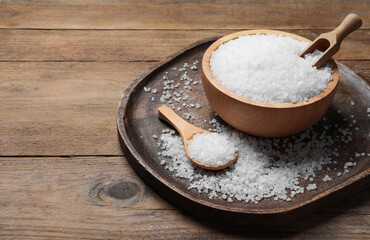 Bowl, spoon and scoop with natural sea salt on wooden table. Space for text