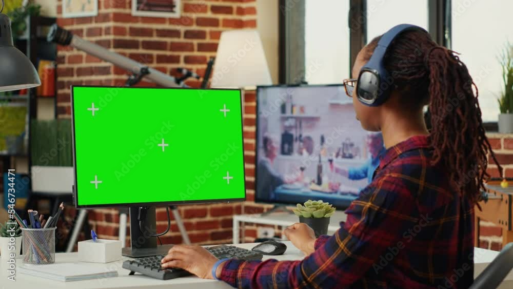 Poster female freelancer wearing headphones and using greenscreen on computer desktop, sitting at desk and 