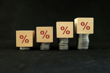Increase interest rate, tax rise and inflation concept. Wooden blocks with percentage sign in increasing stack of coins.