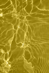 Defocus blurred transparent gold colored clear calm water surface texture with splashes and bubbles. Trendy abstract nature background. Water waves in sunlight with copy space. Gold watercolor shining