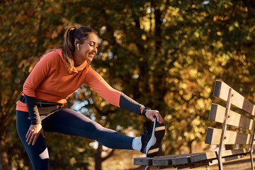 Happy athletic woman stretching her leg on bench in park.