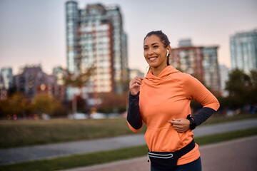 Happy athletic woman listens music on earphones while jogging in park.