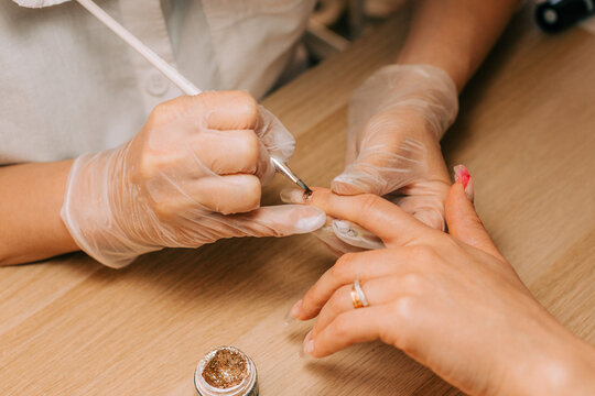 Manicurist using brush and golden glitters for nail design