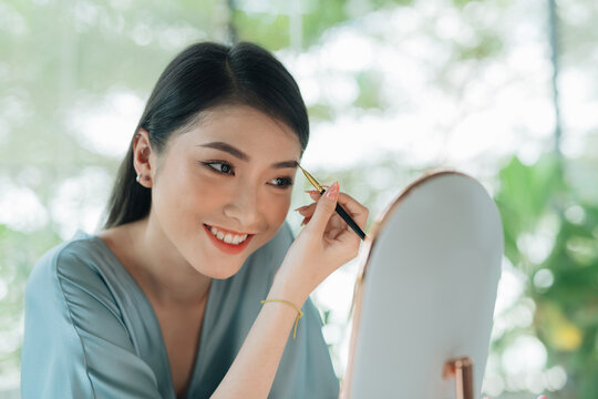 Asian woman drawing eyebrow to her face.