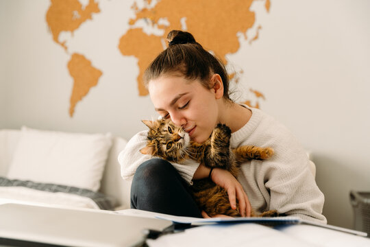 Teenager playing with her cat while studying 