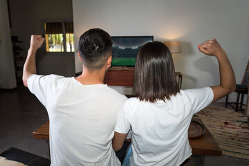 young couple sitting on their couch at home watching a football game, gol