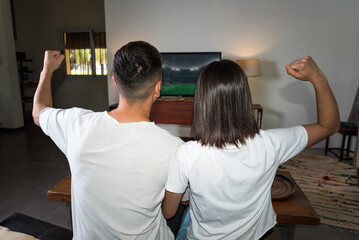 young couple sitting on their couch at home watching a football game, gol © Jezabel