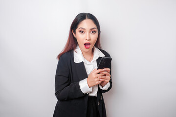 Surprised Asian businesswoman wearing black suit holding her smartphone, isolated by white background