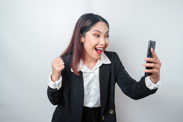 A young Asian businesswoman with a happy successful expression wearing black suit and holding smartphone isolated by white background