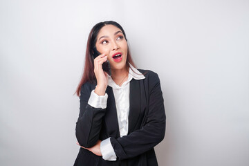 A portrait of a happy Asian businesswoman is smiling while talking on phone call wearing a black suit isolated by a white background