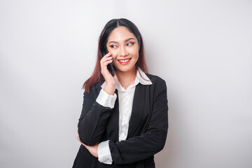 Fototapeta na wymiar A portrait of a happy Asian businesswoman is smiling while talking on phone call wearing a black suit isolated by a white background