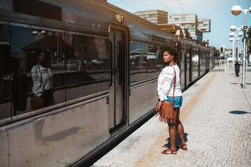 Fototapeta premium View of a beautiful mature plus-size Hispanic woman standing on a railroad platform in front of the a railway suburban train and waiting when the doors open and will be a possibility to enter it