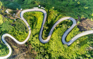 Aerial video top view drone road photo over green mountains with white fog floating and paths exciting steep road way of travel	
