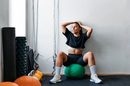 Woman Sitting on Medicine Ball in Gym