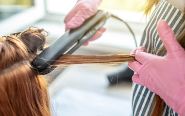 Master is running a iron through the client's hair for keratin straightening. Process of hair care...