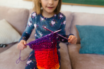 young girl knits a colorful scarf