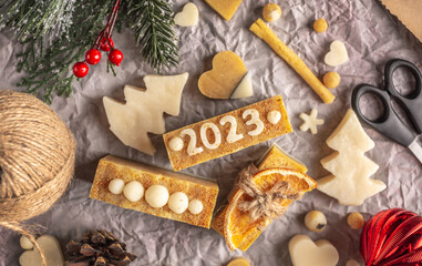 Christmas decor, handmade soap with the number 2023, wrapping paper and ribbon on the paper background top view. Concept of packaging gifts for the New Year and a festive mood