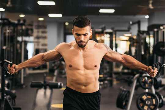 Shirtless strong man training pulley crossover in the gym.
