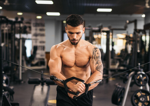 Shirtless strong man training pulley crossover in the gym.