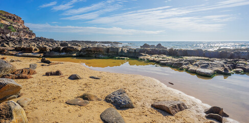 Fototapeta na wymiar Pool of salt water on the rocky Headland at Point Arkwright with cloudy sky and a sunlit ocean.