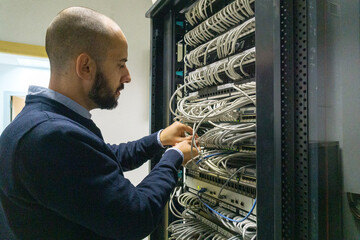 Computer technician man checking cables in a communications rack