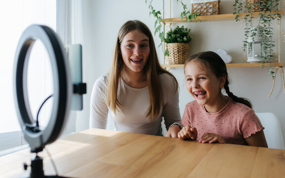 Smiling young sisters recording video on smartphone