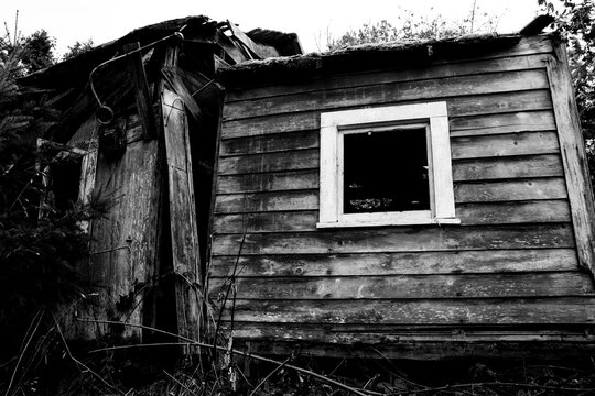 A black and white image of a very old and run down house with a white wooden window. 