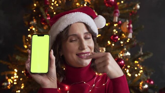 Woman in red sweater and Santa's hat holding a mobile phone with a green screen