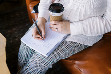 Woman holding beverage and writing down a to do list at a cafe 