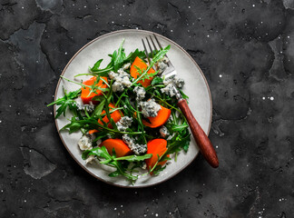 Persimmon, arugula, gorgonzola salad - delicious vegetarian seasonal snack, appetizer on a dark background, top view