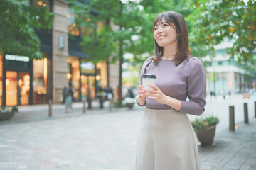 コーヒーカップを持って街を歩く女性