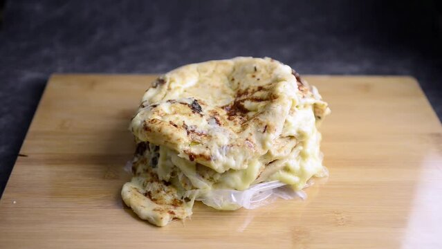 Video of Hand placing a pupusa on a stack of pupusas on a wooden board and dark marble background