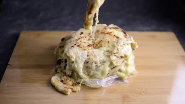 Video of Hand picking a pupusa from a stack of pupusas on a wooden board and dark marble background