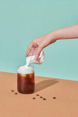 Female hand pouring shaked and foamed ice coffee to glass