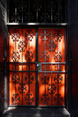 Sunlit orange door behind iron gate