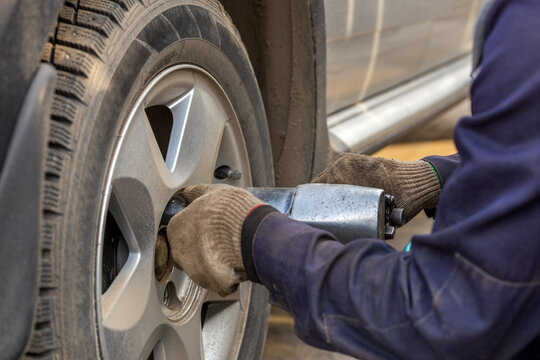 Hands Of Automotive Mechanic Unscrewing Nuts With Pneumatic Impact Wrench During Car Wheels Season Changing