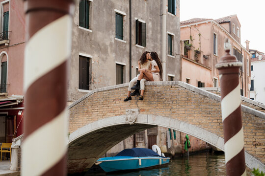 Women kissing while sitting on a bridge in Venice