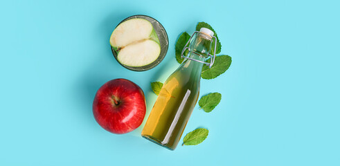 Bottle of apple cider vinegar, mint leaves and fruits on blue background