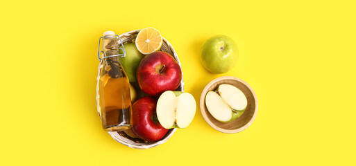 Basket with bottle of apple cider vinegar and fruits on yellow background
