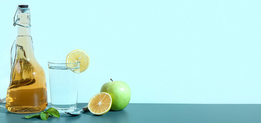 Bottle of apple cider vinegar and glass of water on light blue background with space for text
