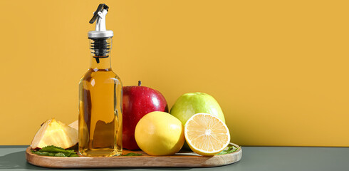 Bottle on apple cider vinegar and fruits on table near color wall