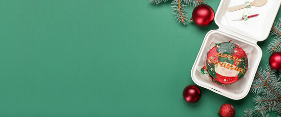 Plastic lunch box with tasty bento cake, fir branches and Christmas balls on green background with space for text