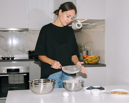 Young woman confectioner sifting flour through a sieve