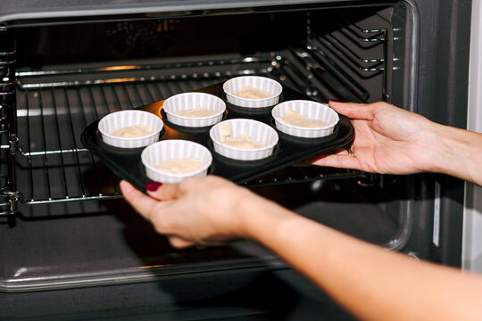 Women's hands put a mold with cupcakes in a preheated oven.